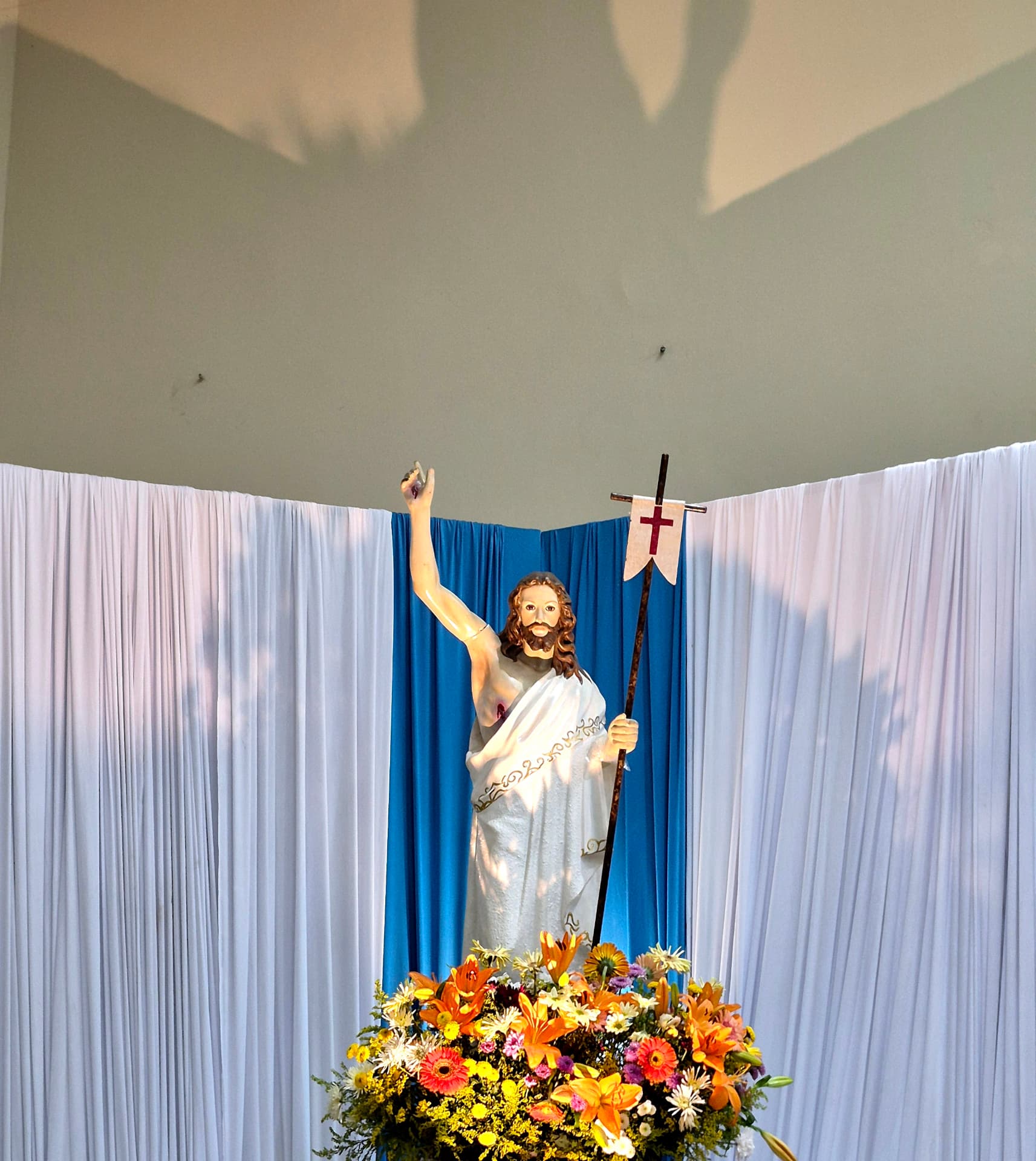 Imagem do Cristo Ressuscitado com flores diante do cortinado